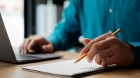 Un homme regarde son ordinateur et prend des notes avec un crayon et du papier