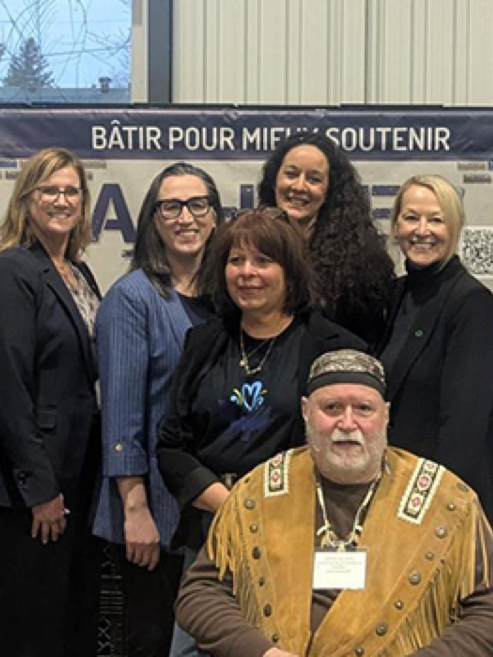 Groupe de personnes réunies devant des bannières d’Aux Sources du Bassin de Chambly, dans un espace intérieur, dont l’une est assise au premier plan.