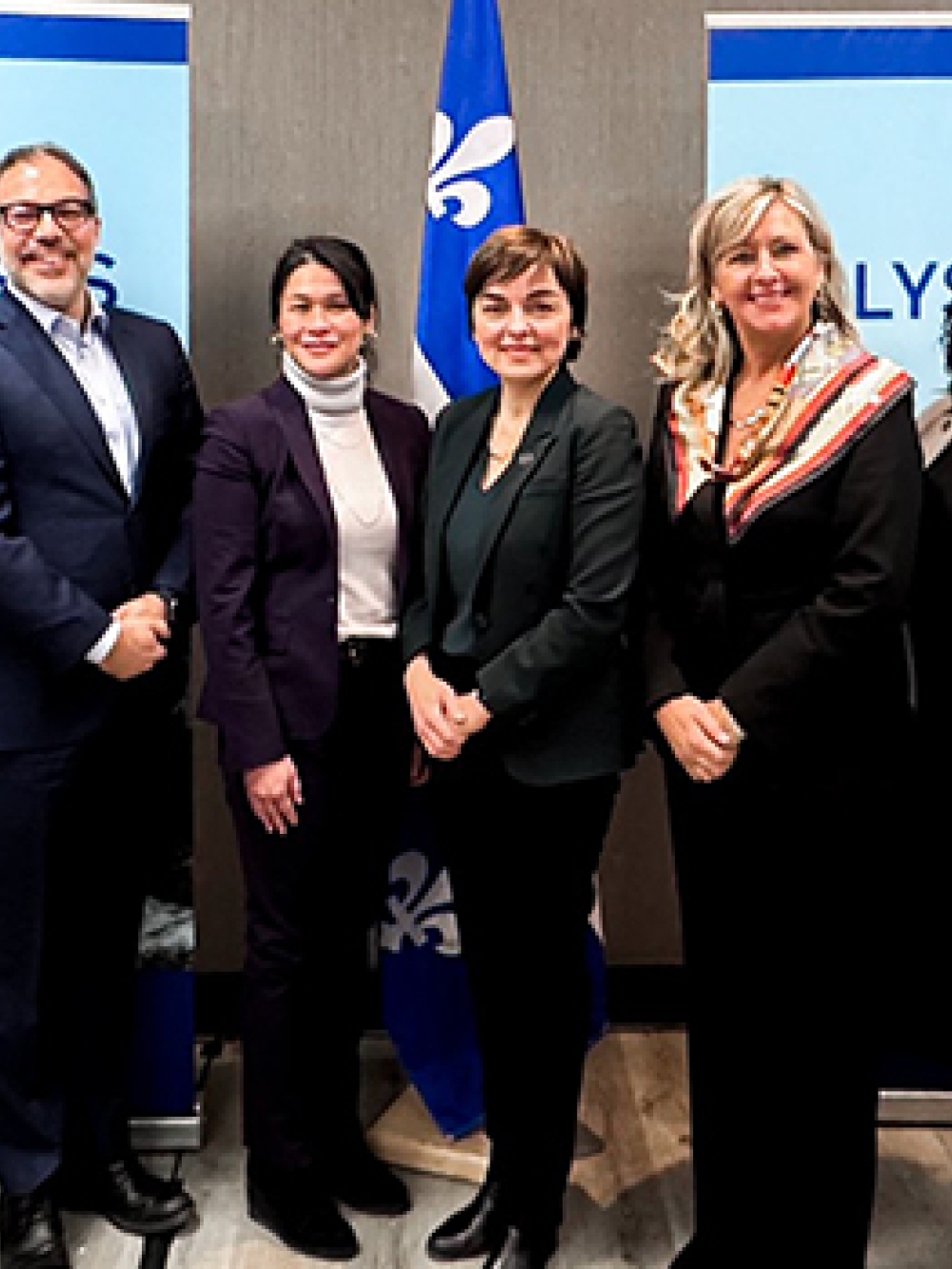 Groupe de personnes debout dans une salle de conférence devant deux panneaux ELYSIS et un drapeau du Québec, posant pour une photo officielle.