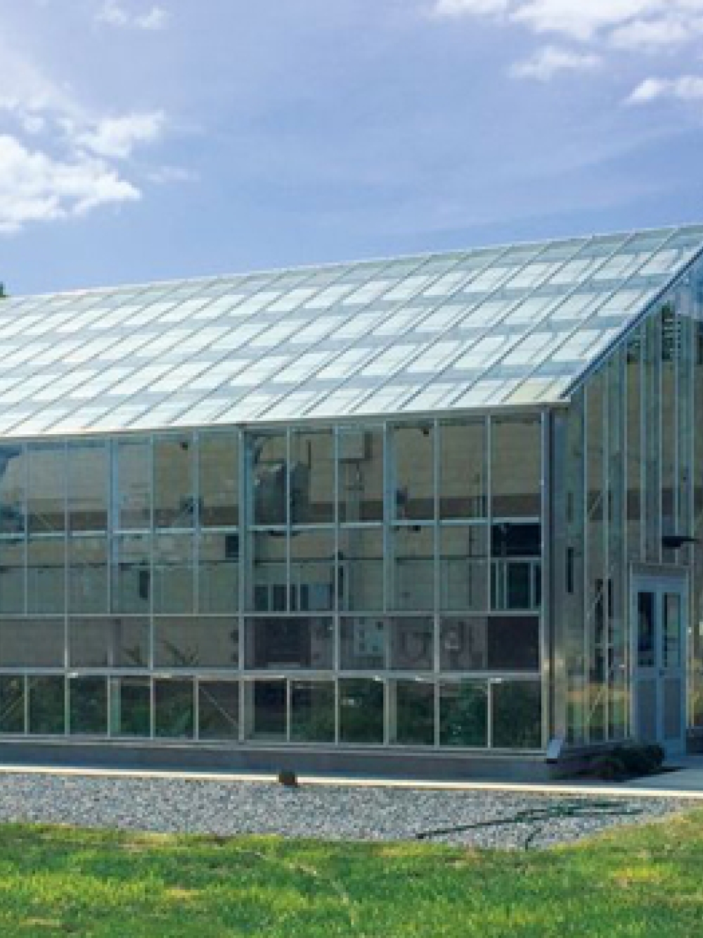 Bâtiment industriel moderne avec une grande serre vitrée à l’avant, situé sur un terrain gazonné, avec un réservoir blanc portant le logo « WaterHub » en arrière-plan.