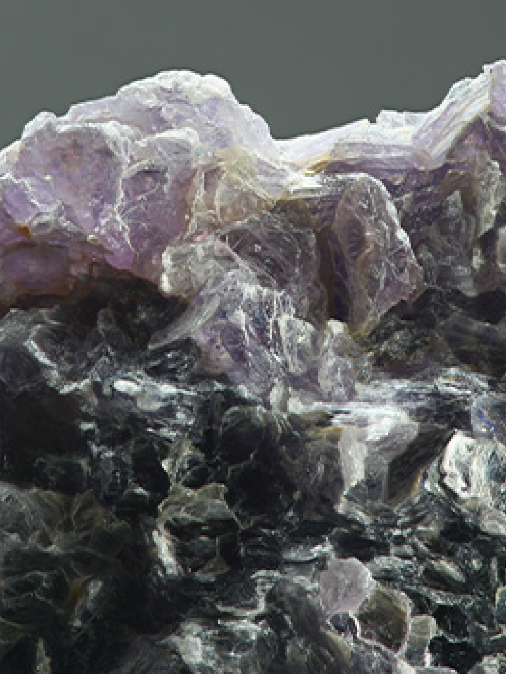 Grosse roche brute composée de cristaux aux teintes violettes, noires et blanches, montrant une texture minérale détaillée.