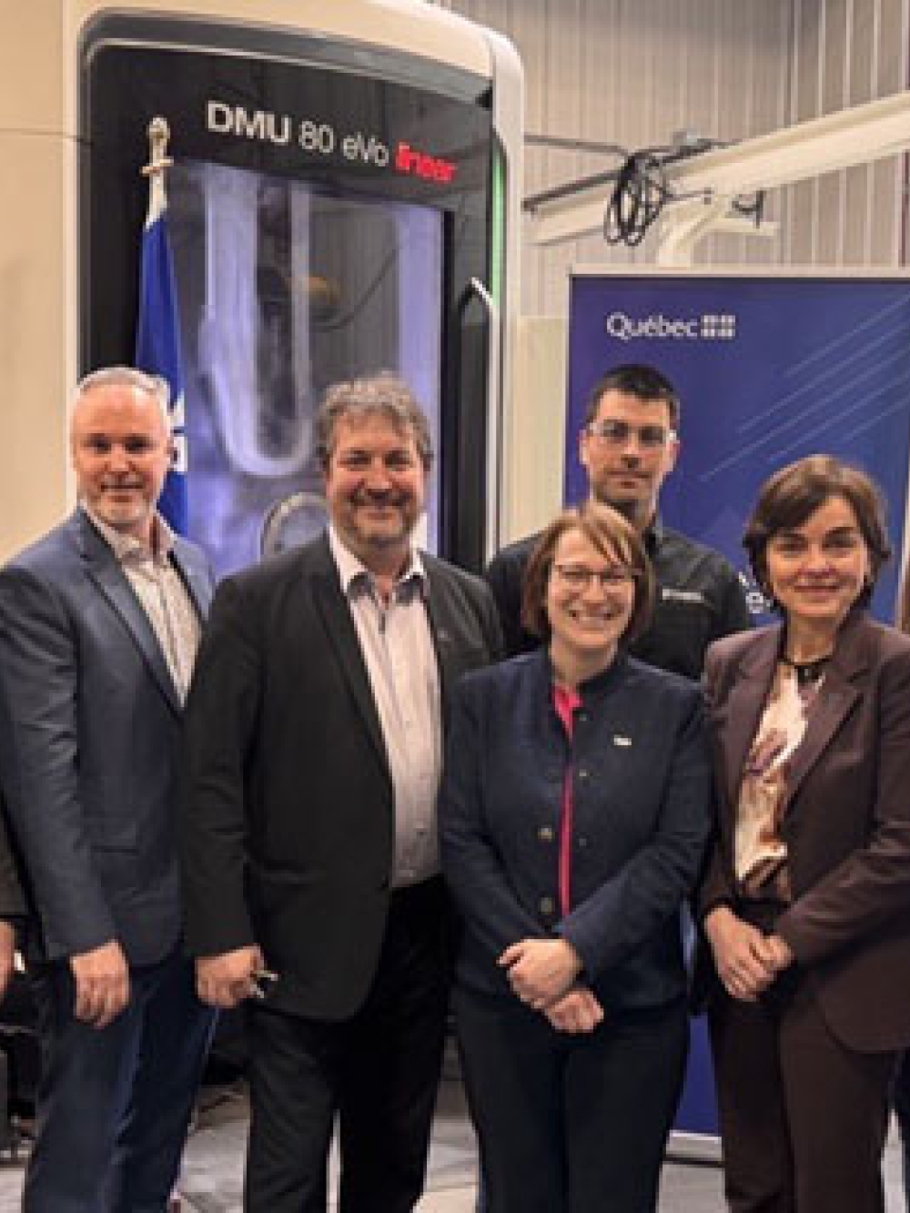 Groupe de personnes debout dans une usine devant des équipements industriels et une bannière du gouvernement du Québec.