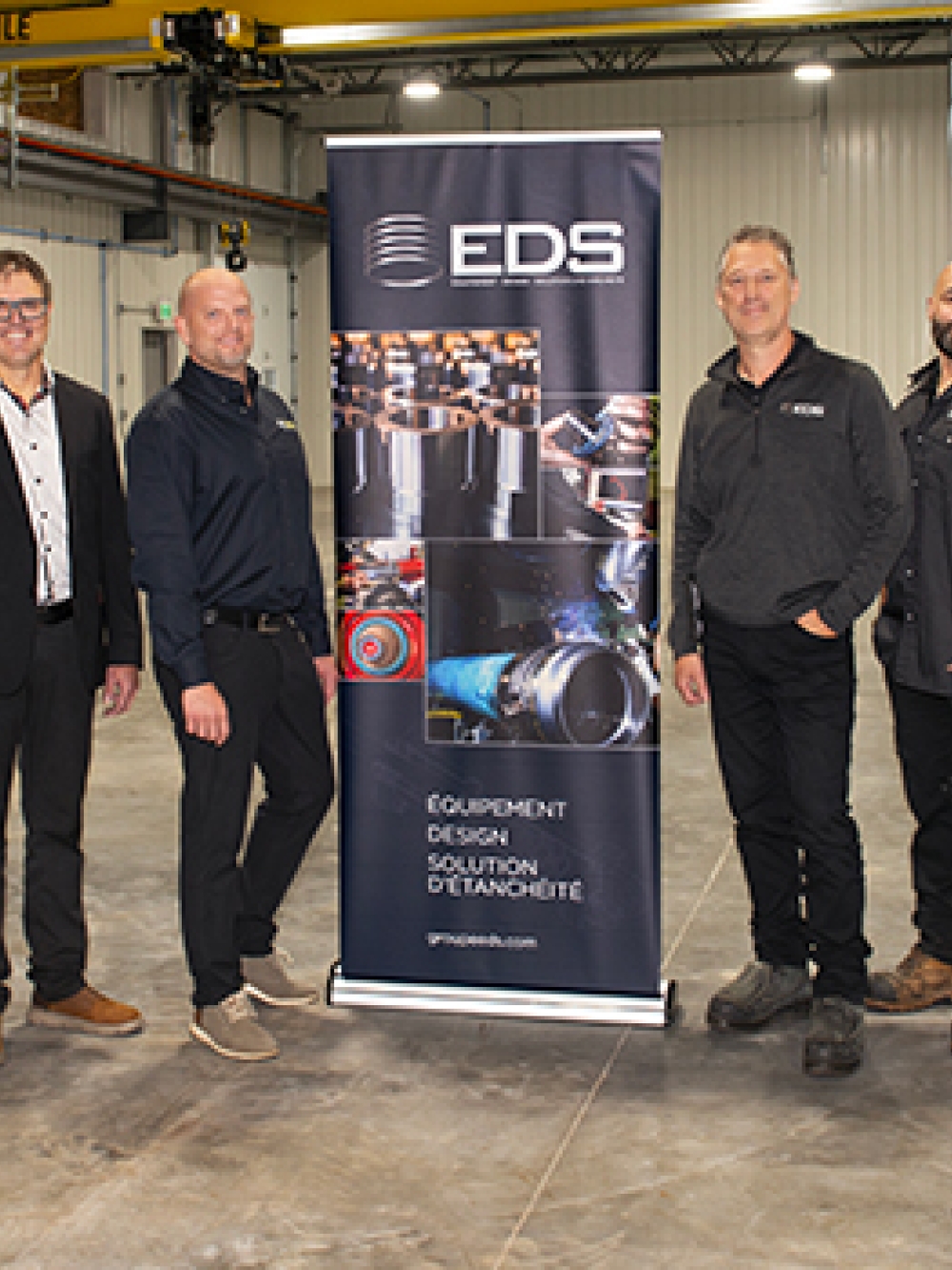 Groupe de personnes debout dans un vaste atelier industriel, de part et d’autre d’une bannière EDS présentant des images d’équipement et de solutions d’étanchéité.