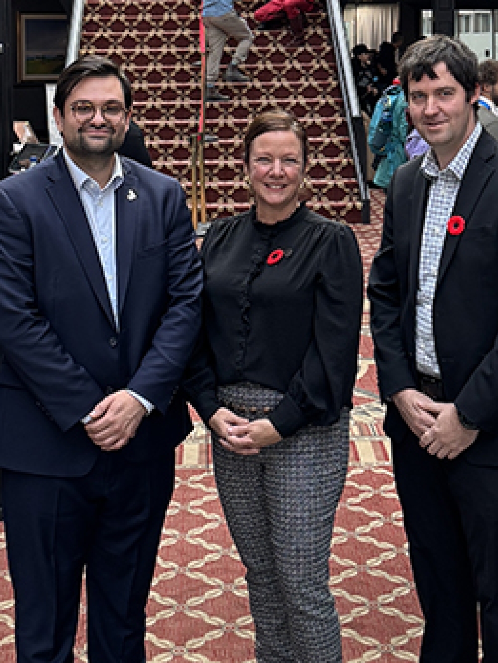 Groupe de personnes posant dans un hall d’événement, entouré de bannières promotionnelles et de participants, lors d’une activité officielle.