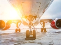 ue de face d’un avion sur une piste d’aéroport, montrant le train d’atterrissage, les deux moteurs et un soleil éclatant se reflétant sur le fuselage.