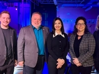 Groupe de cinq personnes posant dans une salle éclairée en bleu, avec un drapeau du Québec et des affiches visibles en arrière‑plan.