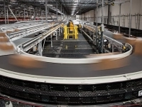 Système automatisé de convoyeurs industriels transportant des colis dans un grand entrepôt logistique équipé de structures métalliques et de mécanismes de tri.