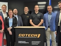 Groupe de personnes debout derrière un lutrin portant le logo de Cotech, accompagné de mentions sur la fabrication d’équipements de déneigement, d’excavation et agricoles, dans une salle de présentation.