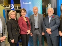 Groupe de personnes en tenue professionnelle posant dans un atelier industriel, devant un panneau bleu portant le logo du Québec et des équipements de machinerie en arrière-plan.