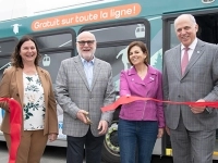 Groupe de personnes participant à une cérémonie d’inauguration devant un autobus, tenant un ruban rouge pour une coupe officielle.