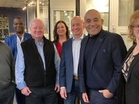 Groupe de sept personnes posant à l’intérieur d’un espace industriel ou commercial, devant des fenêtres et des présentoirs.