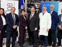 Groupe de personnes debout dans une usine, posant devant des bannières de l’entreprise et du gouvernement du Québec lors d’un événement officiel.