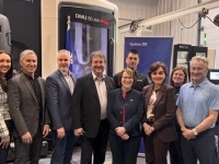 Groupe de personnes debout dans une usine devant des équipements industriels et une bannière du gouvernement du Québec.