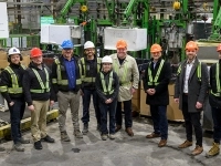 Groupe de personnes portant des casques et des équipements de sécurité dans une usine, posant devant des machines industrielles.