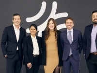 Groupe de cinq personnes debout devant un mur sombre affichant un grand logo blanc.