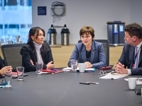 Personnes assises autour d’une grande table de réunion, discutant et prenant des notes lors d’un échange formel dans une salle de conférence.