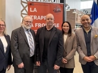 Groupe de cinq personnes posant dans un commerce de fromagerie, devant une affiche « La Trappe à Fromage » et un drapeau du Québec, avec des étagères de produits à droite.