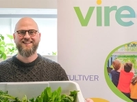 Personne tenant un bac de légumes frais devant une bannière de Vireo, dans un environnement d’agriculture urbaine hydroponique.