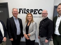 Groupe de personnes debout devant un mur portant le logo de FilSpec, dans un espace d’accueil d’entreprise.