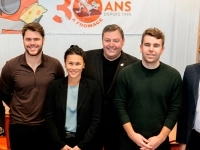 Groupe de personnes posant à l’intérieur d’un commerce, devant une bannière du 30e anniversaire de La Trappe à Fromage et des étagères remplies de produits.